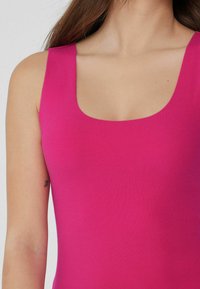 Top sin mangas de color fucsia con escote cuadrado, de tejido suave y diseño ajustado, que resalta el escote y la línea de los hombros.