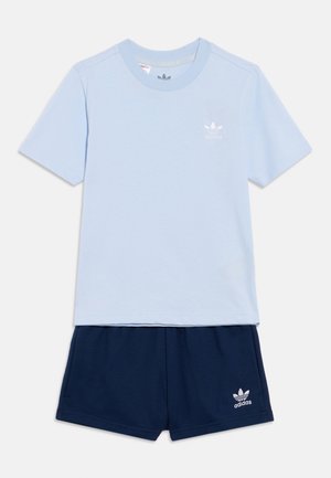 Camiseta de algodón azul claro combinada con shorts azul marino. La camiseta tiene un pequeño logo blanco de Adidas; los shorts llevan un logo a juego en el dobladillo.