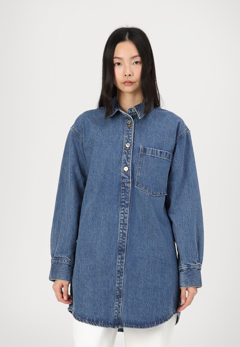 Denim srajca v svetlo modri barvi, z gumbnico spredaj, žepom na prsih, dolgimi rokavi in zaobljenim robom. Teksturna, brez okraskov.