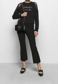 Sudadera negra con detalles de encaje en las mangas y el texto "PINKONESS CALLING". Pantalones de pierna acampanada negros y zuecos de tacón alto negros con hardware dorado.