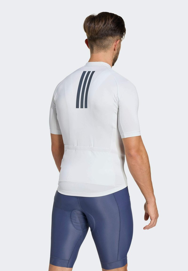 Weißes kurzärmeliges Radtrikot mit hohem Kragen und grauen Streifen auf der Rückseite. Kombiniert mit navyblauen Radhosen.