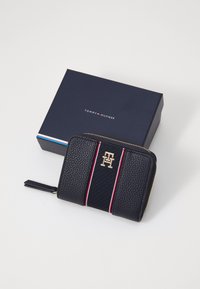 Navy leather wallet with gold logo; features red and white stripe detail. Comes in a dark blue branded box. Zipper closure with a wrist strap.