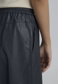 Jupe en cuir gris foncé avec une taille élastique et une poche latérale, mettant en avant une texture lisse et un design épuré.