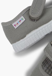 Scarpa in tela grigia con suola bianca, fascia in Velcro e etichetta del marchio colorata. Presenta un motivo testurizzato sulla parte superiore e una fodera a scacchi.