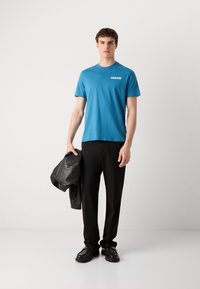 T-shirt di cotone blu a maniche corte e collo rotondo, con il logo bianco di Calvin Klein. Abbinato a pantaloni e scarpe nere.