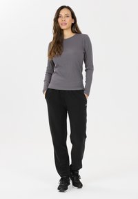 Grijze langemouwen ribgebreide top gecombineerd met zwarte sweatpants. De outfit heeft een elastische tailleband en een losse pasvorm, afgewerkt met zwarte sneakers.