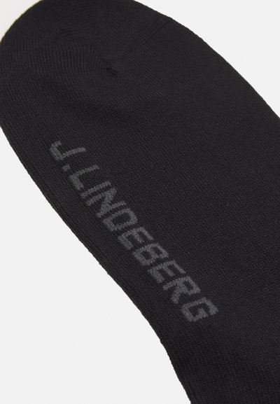 Calcetín negro con textura acanalada y un logo impreso "J. LINDEBERG" en gris en el lateral. Acabado suave y forma afinada en la punta.