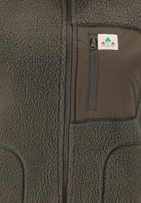 Fleece vest in dark green with a smooth front panel. Features a zippered pocket, side pockets, and a logo patch on the chest.