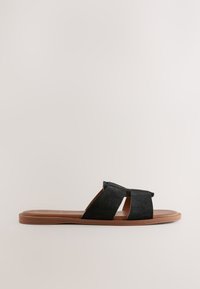Sandale mule en daim noir avec deux brides croisées. Semelle marron flexible, design à bout ouvert et silhouette minimaliste.