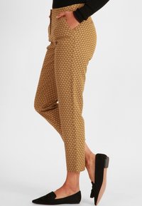 Pantalons brun à motif avec une silhouette ajustée, dotés de poches latérales et d'une texture lisse. Associés à des chaussures plates noires.