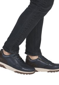 Zapatillas de piel azul oscuro con un acento marrón, que cuentan con una lengüeta texturizada, cierre de cordones y una cremallera lateral. Suela curvada y ligera.