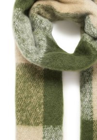 Sciarpa a scacchi verde e beige realizzata in morbida lana testurizzata, con sezioni di diverse tonalità e motivi, avvolta in un anello.