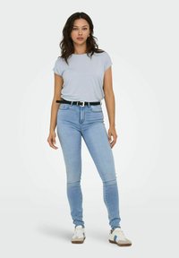 Top de manga corta azul claro, jeans ajustados azul oscuro, cinturón negro y zapatillas blancas con detalles azules. Conjunto de ropa simple y casual.