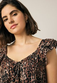 Blus med leopardmönster i mjukt tyg med volangärmar och V-ringning. Färgerna inkluderar brun, svart och kräm.