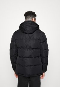 Czarna kurtka puchowa z kapturem, posiadająca poziome pikowane sekcje i gładkie, matowe wykończenie. Odpowiednia na zimną pogodę.