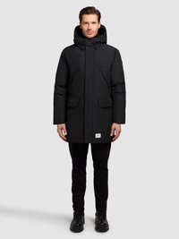 Parka negra aislada con capucha desmontable, cierre de cremallera y broches a presión, dos bolsillos delanteros y una pequeña etiqueta en el dobladillo inferior.