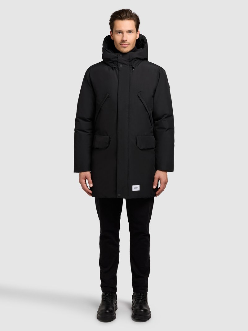 Parka negra aislada con capucha desmontable, cierre de cremallera y broches a presión, dos bolsillos delanteros y una pequeña etiqueta en el dobladillo inferior.