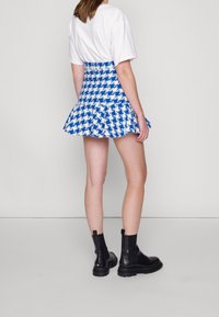 Falda mini a cuadros en azul y blanco con dobladillo acampanado, combinada con una camiseta blanca y botas negras hasta el tobillo. Tejido suave, cintura ajustada.