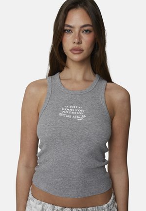 Młoda kobieta z długimi brązowymi włosami, ubrana w szary, bezrękawnik z białym napisem: "2011 Good For Nothing British Atelier MMXI."