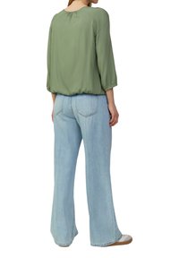 Grüne, leichte Bluse mit gerafftem Rückendetail, kombiniert mit hellblauen, weit geschnittenen Jeans mit Gesäßtaschen und lockerer Passform.