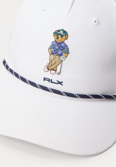 Λευκό καπέλο με κεντημένη αρκούδα που φοράει γκολφ ένδυμα και κρατά ένα γκολφ ρόπαλο, πάνω από τα γράμματα "RLX" στον μπροστινό πίνακα.