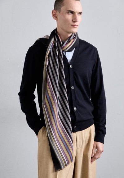 Stripet skjerf i grått, gult og rødt, brukt over en mørk cardigan. Har knapper, v-hals, og en avslappet passform med beige bukser.