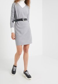 Robe grise en tricot avec un col en V, des manches longues et une ceinture noire. Associée à des baskets noir et blanc au design sportif.