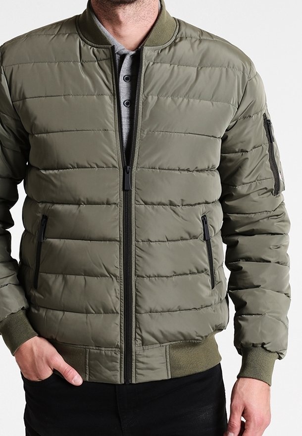 Chaqueta bomber acolchada verde oliva con cierre de cremallera en el frente, cuello acanalado, dos bolsillos laterales y un bolsillo con cremallera en la manga izquierda.