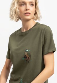 Olivengroene katoenen t-shirt met een grafische print van een zittende figuur omringd door loof, korte mouwen en een klassieke ronde hals.