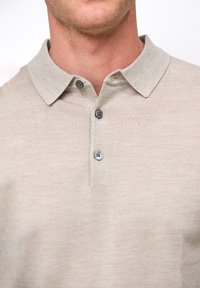 Polo beige confeccionado en tejido de punto texturizado, con cuello, tapeta con tres botones y sutiles detalles de costura.