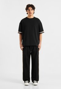 Juodas medvilnės marškinėlis su dekoratyviais apvadais ant rankovių, derinamas su juodais sportiniais šortais su šoninėmis detalėmis ir raišteliu. Į komplektą įeina sportbačiai.