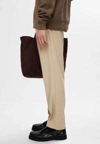 Pantalones de pierna ancha beige hechos de tela suave, combinados con mocasines negros con suela texturizada y un bolso tote marrón oscuro.