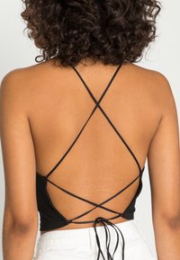 Černý crop top s tenkými, křížovými ramínky na zádech, s přiléhavým střihem a jemnou texturou, kombinovaný se světlými šortkami.