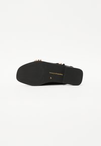 Svart sandal med en teksturert såle, med gullfargede detaljer og flat profil. Størrelse 37 trykket på sålen.