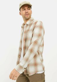 Geruit overhemd in beige met een patroon van rood en lichtbruin. Lange mouwen, borstzak en een ontspannen pasvorm. Gepaard met kaki broek.