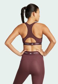 Bordeaux sportbeha met een racerback ontwerp en uitsnijding, gecombineerd met bijpassende high-waisted leggings. Beide hebben een "Adidas Techfit" band.