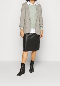 Rutigt blazern, grön tröja, vit skjorta, svart läderkjol och svarta ankelskor. Strukturerade material med en väl avvägd design.