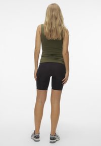 Olivgrön linne och svarta högmidjade cykelshorts. Modell sedd bakifrån, med en figurnära passform och platta sömmar.