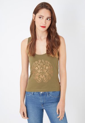 Camiseta sin mangas de color verde oliva con escote redondo y un diseño floral dorado en la parte delantera, combinada con pantalones vaqueros azules claros.