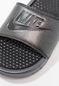 Sandale noire Nike slide avec semelle intérieure texturée et bride métallique affichant le logo Nike embossé et le swoosh.
