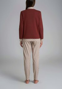 Maglia a maniche lunghe color marrone scuro con colletto, abbinata a pantaloni pigiama a quadri crema e marrone con motivo. Tessuto morbido, vestibilità comoda e dettagli minimali.