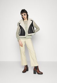 Colete de pele de ovelha preto e creme, blusa de renda de mangas longas, blusa verde-menta, calças largas creme, botas de salto castanhas até ao tornozelo, óculos de sol brancos.