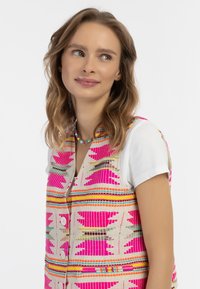 Colorful woven vest featuring bold pink, orange, and yellow patterns. Made of textured fabric with buttons at the front and a layered design.