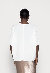 Hvid, letvægts bluse med korte ærmer, rund kant og en midterseam, parret med en skinnende beige nederdel.