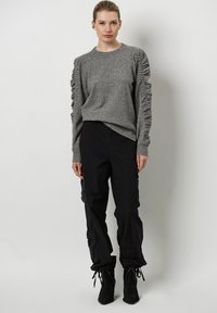 Grijze trui met textuur en gerimpelde mouwen, gecombineerd met zwarte cargo broeken en enkellaarsjes met studaccenten.