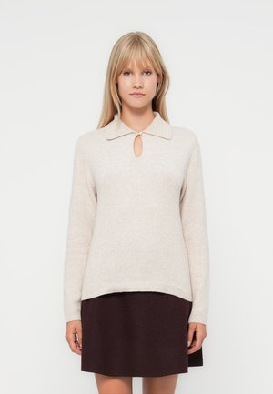 Lys beige genser med krage og nøkkelhull-utrigning, med lange ermer og ribbestrikket kant. Modellen har på seg et mørk burgunder skjørt.