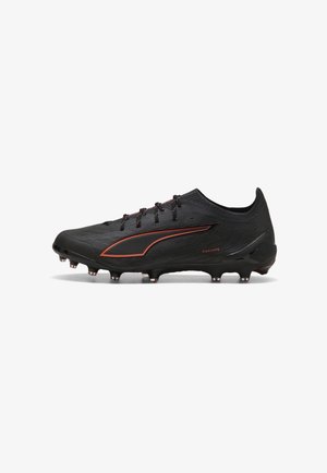 Scarpa da calcio nera con dettagli arancioni e tacchetti sulla suola, con un design con lacci e una superficie testurizzata.