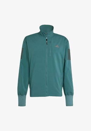 Giacca sportiva teal realizzata in materiale liscio e leggero. Presenta un alto colletto, una chiusura con zip e tre strisce scure sulle spalle.