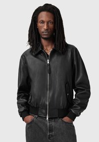 Czarna skórzana kurtka bomberka z zamkiem błyskawicznym z przodu, ściągaczami na mankietach i w pasie. Posiada boczne kieszenie i gładką, błyszczącą fakturę.