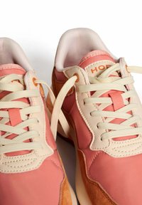 Zapatillas deportivas ligeras en una combinación de colores rosa y naranja, con una mezcla de texturas suaves y de ante, cordones crema y lengüetas acolchadas.